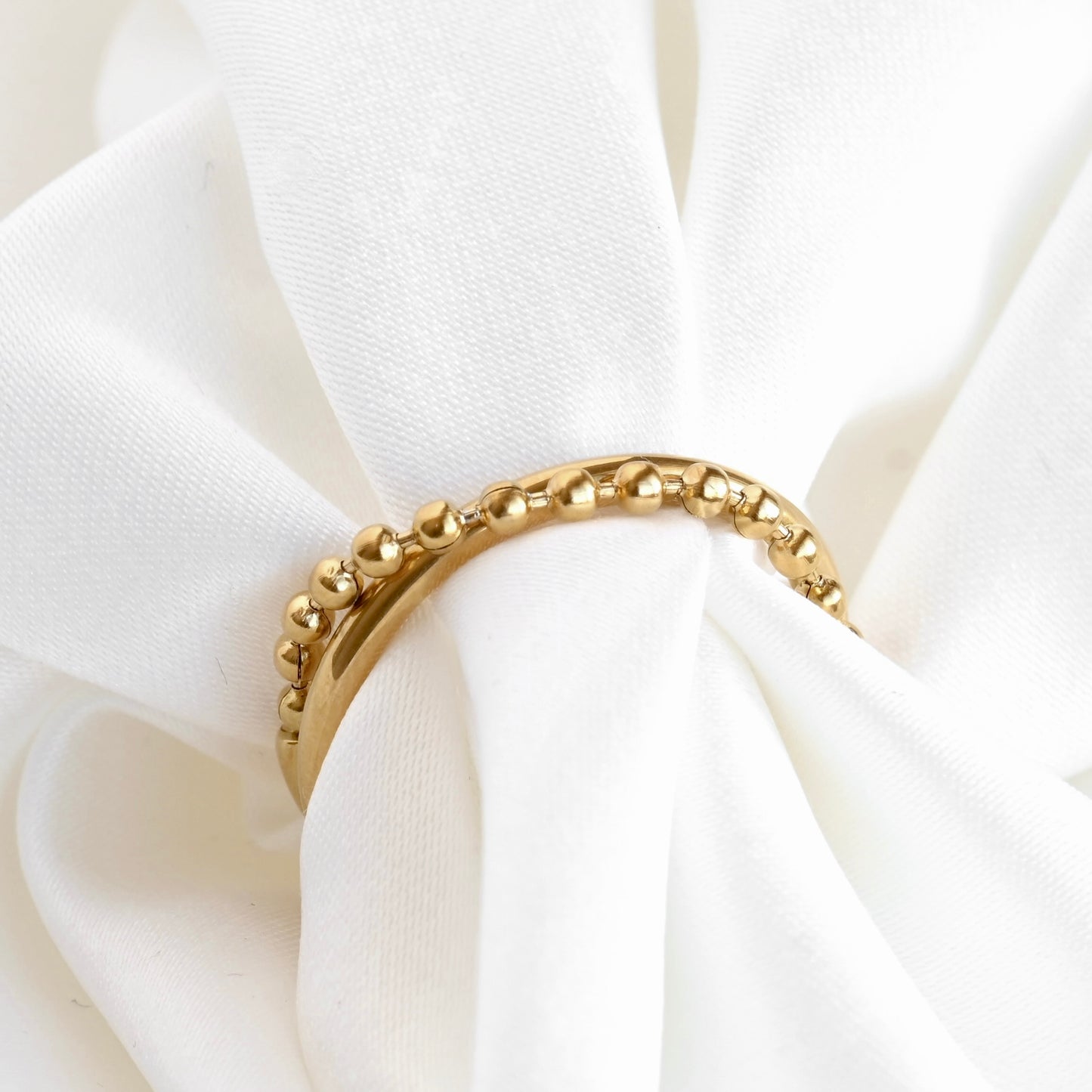 A gold beaded wrap ring displayed on a white fabric napkin.