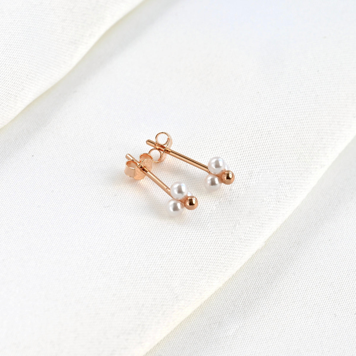 Tope view of rose gold pearl earrings on a white fabric background