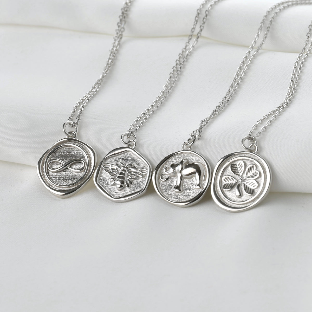Three silver necklaces with circular pendants on a white surface