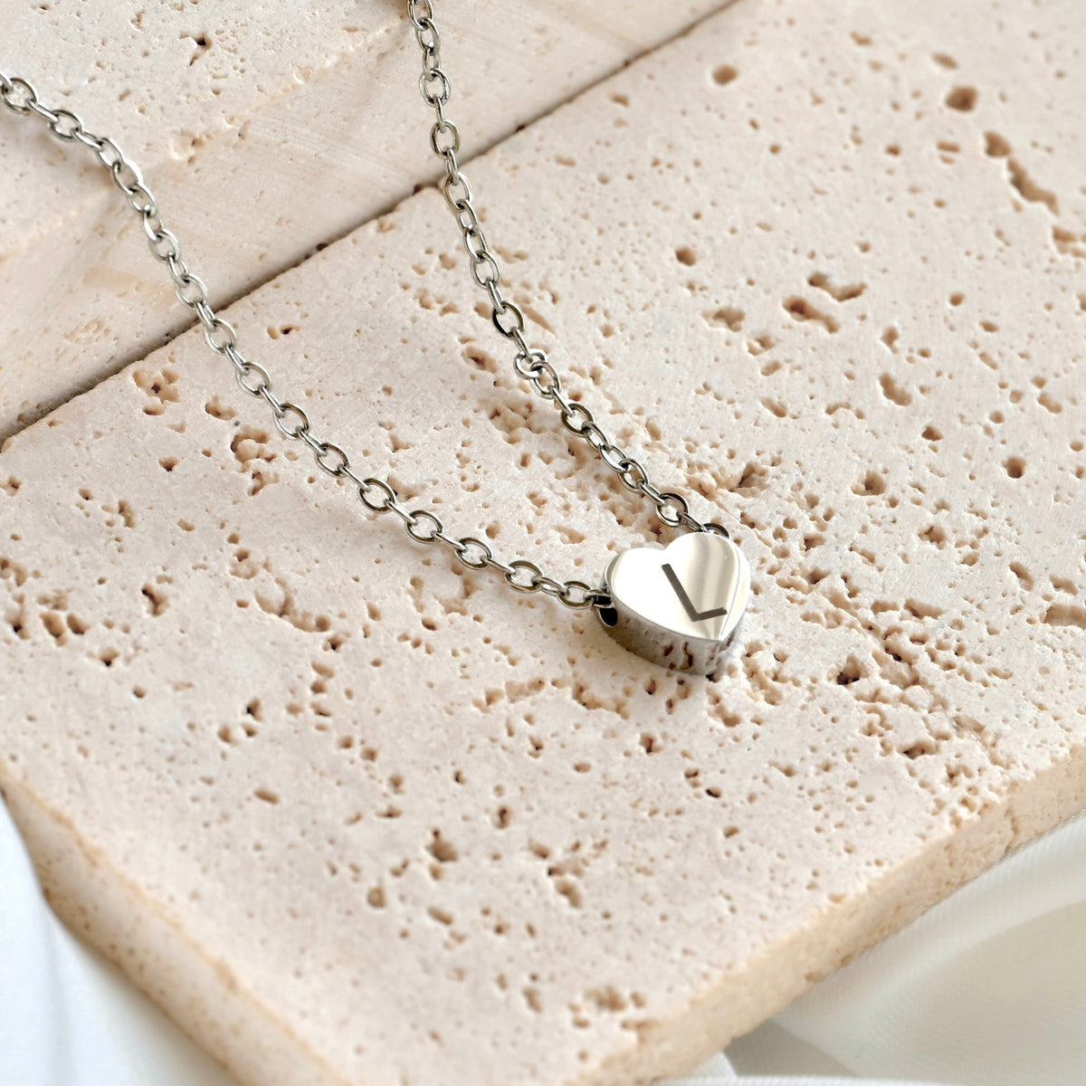 Silver heart necklace with a letter 'L' on a textured stone surface
