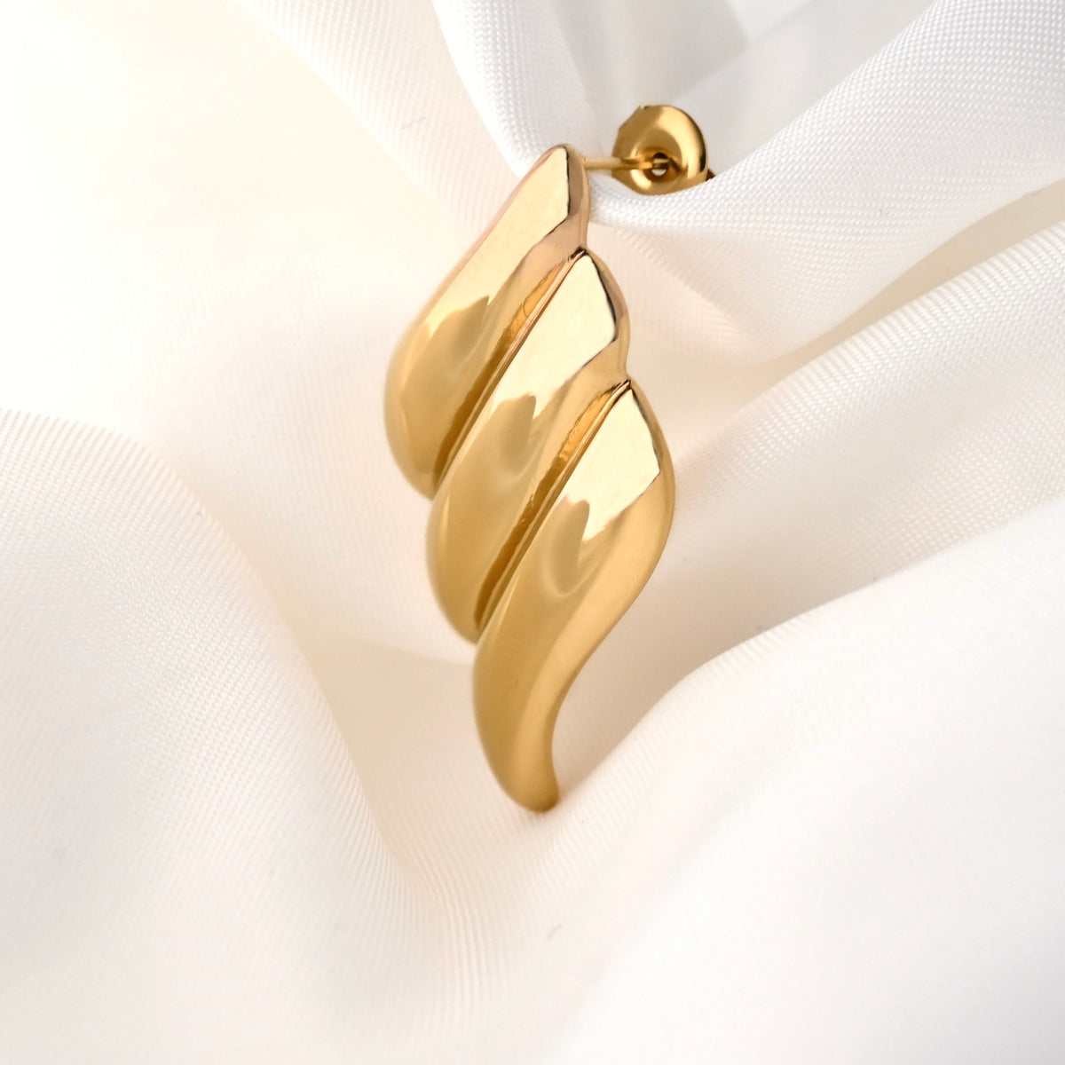 Gold diamond shaped textured drop earrings on a white fabric background