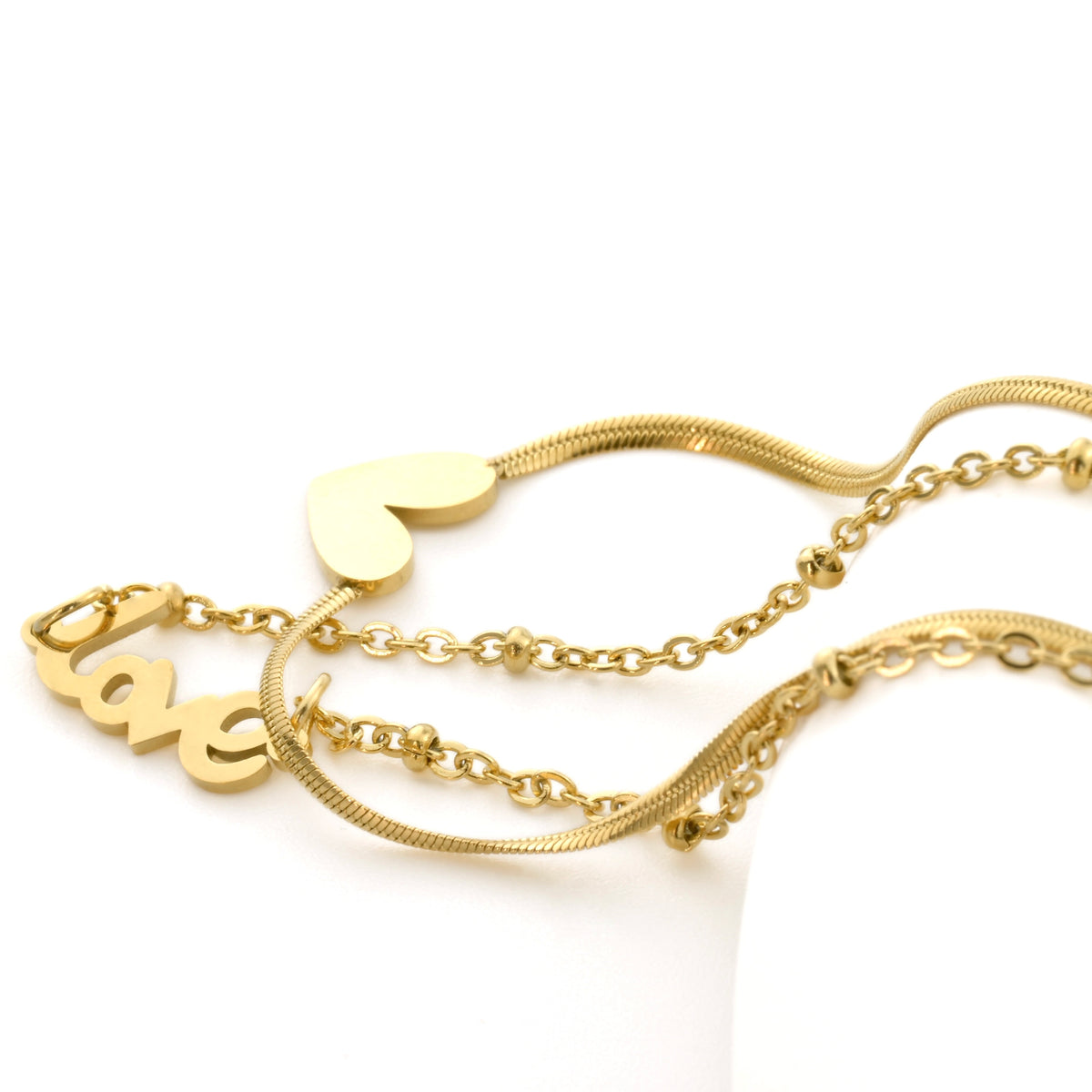 Close-up view of gold anklet's charms: heart and 'love' on a white background