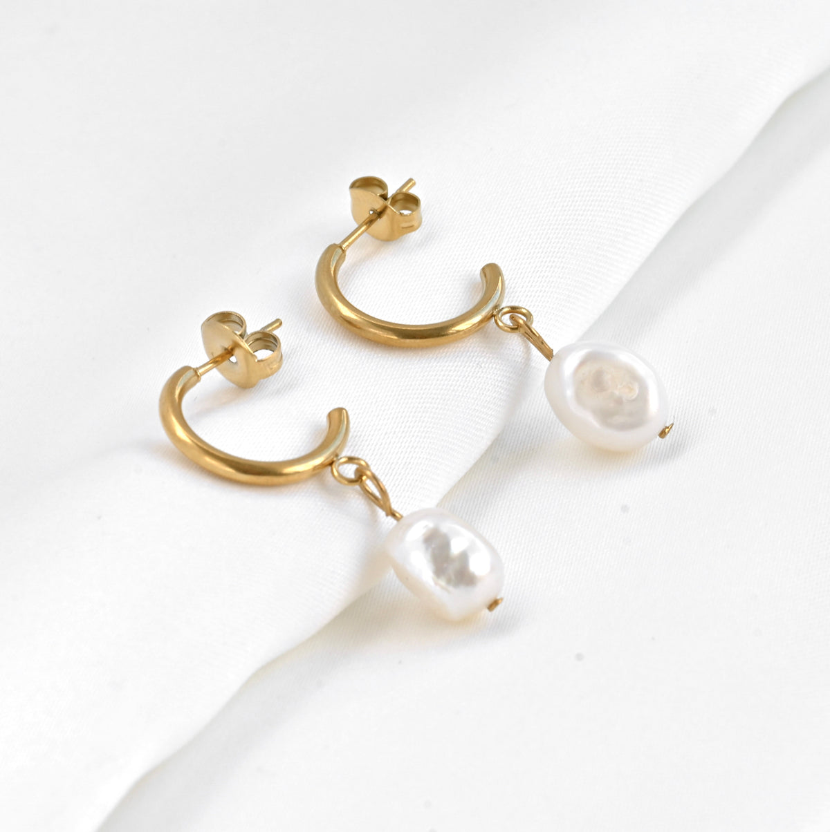 Gold C hoop earrings with freshwater pearl drops on a white background