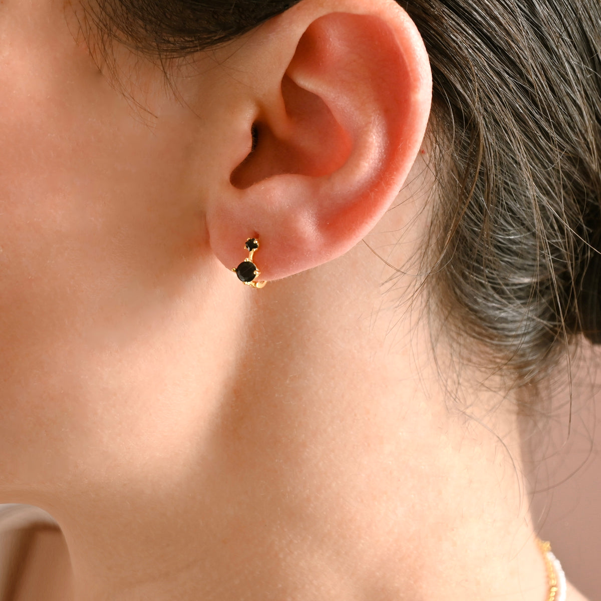 Close-up of an ear wearing a black hoop earring with gold accents.