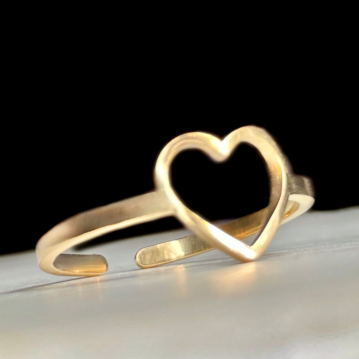 Gold ring with a heart charm and open back on a reflective surface with a black background