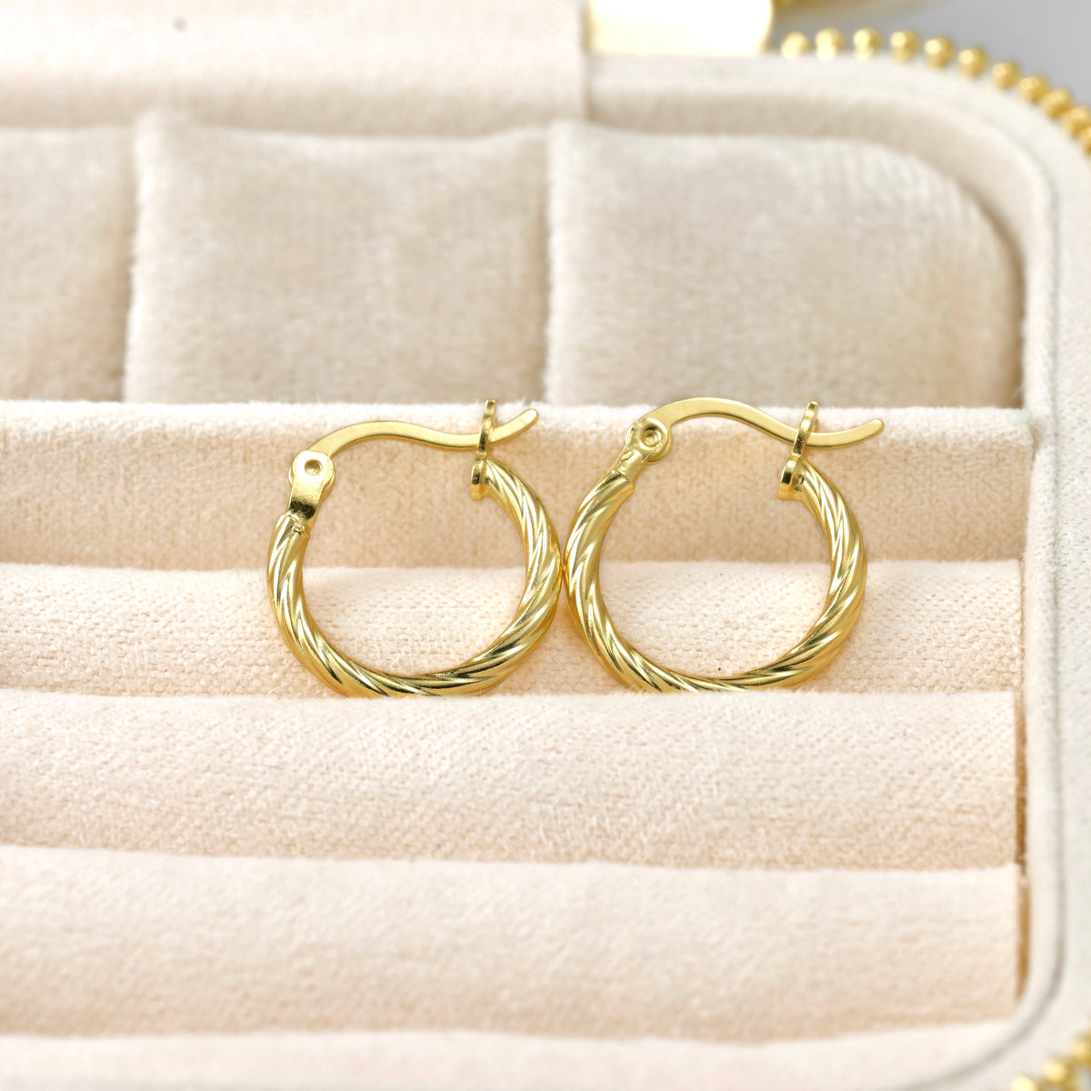 18k Gold thin hoop earrings on a textured beige surface