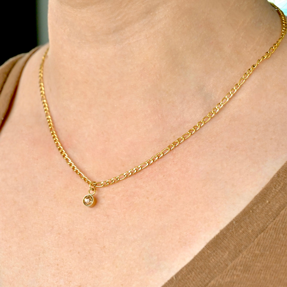 Gold figaro necklace with round november birthstone on a person's neck