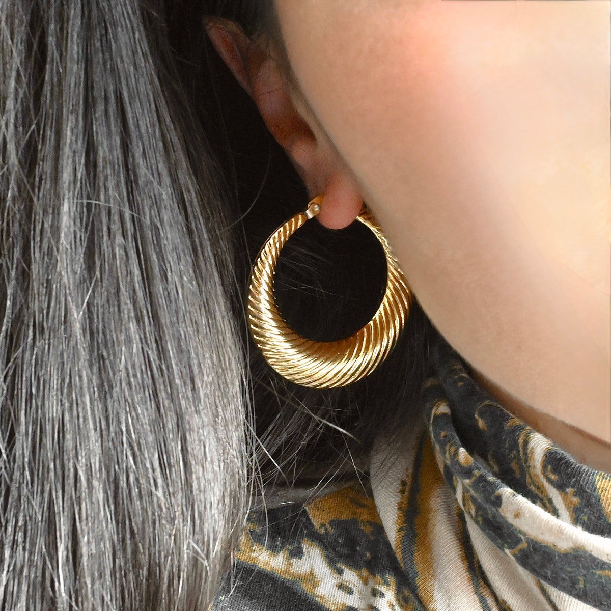 Close-up of a person wearing large gold croissant hoop earrings