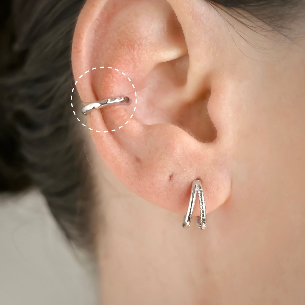Close-up of an ear wearing a silver ear cuff with a blurred background