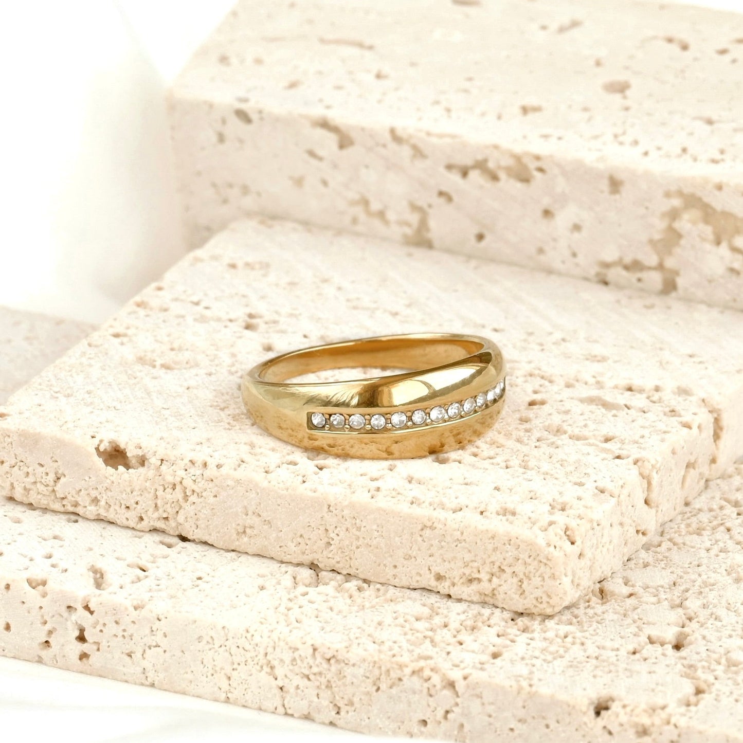 Gold ring with a pave diamond line in the middle on a textured stone surface
