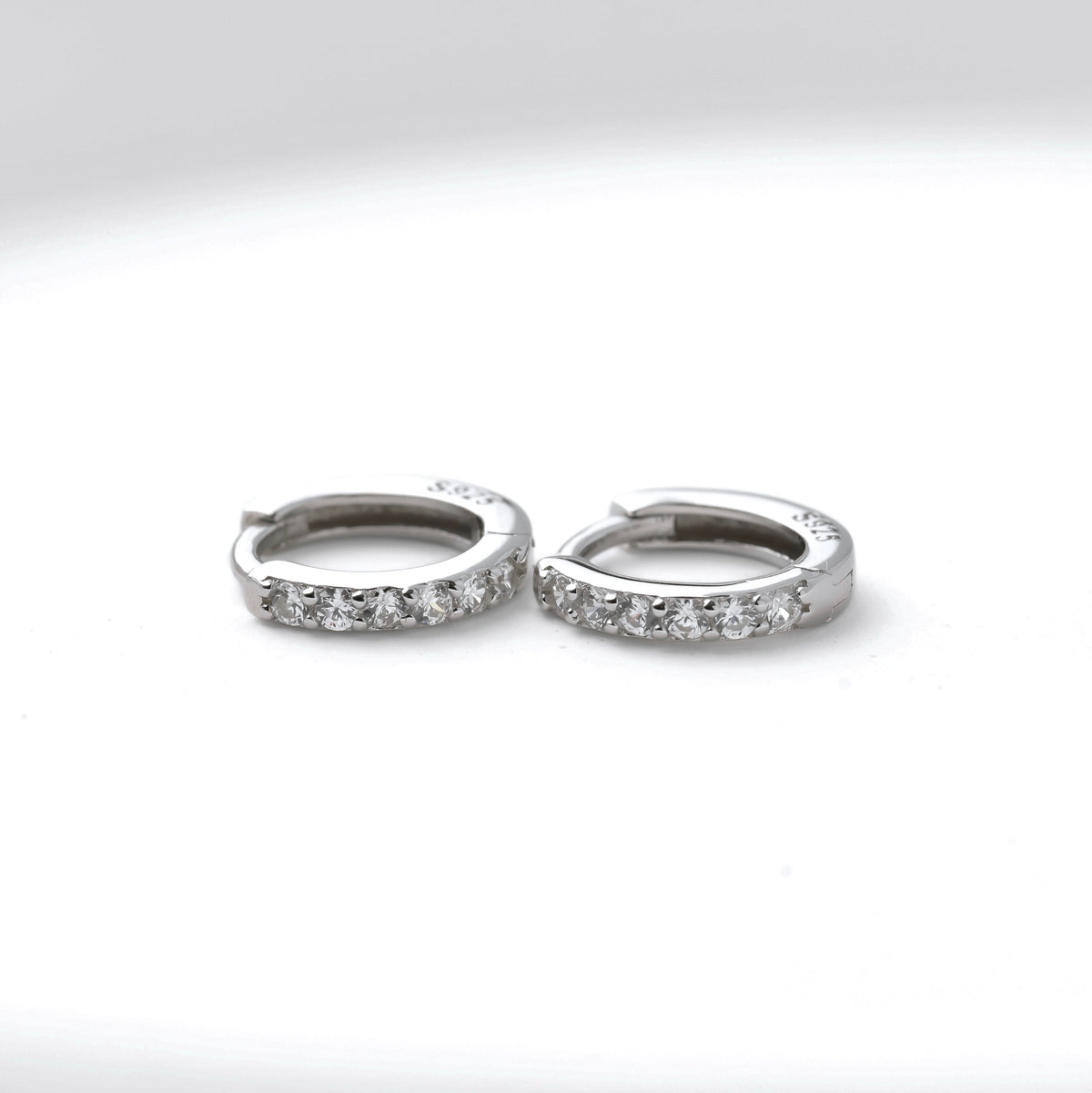 Pair of silver half eternity pave hoop earrings with S925 stamp on a white background