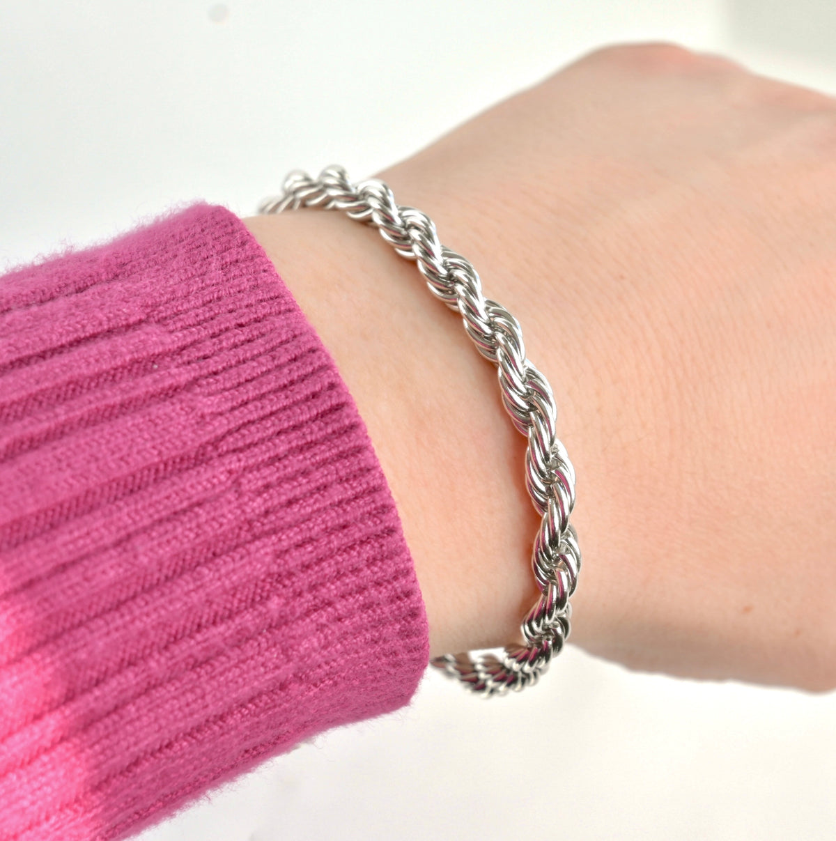 Bold silver rope chain bracelet on a wrist with a pink sleeve against a white background
