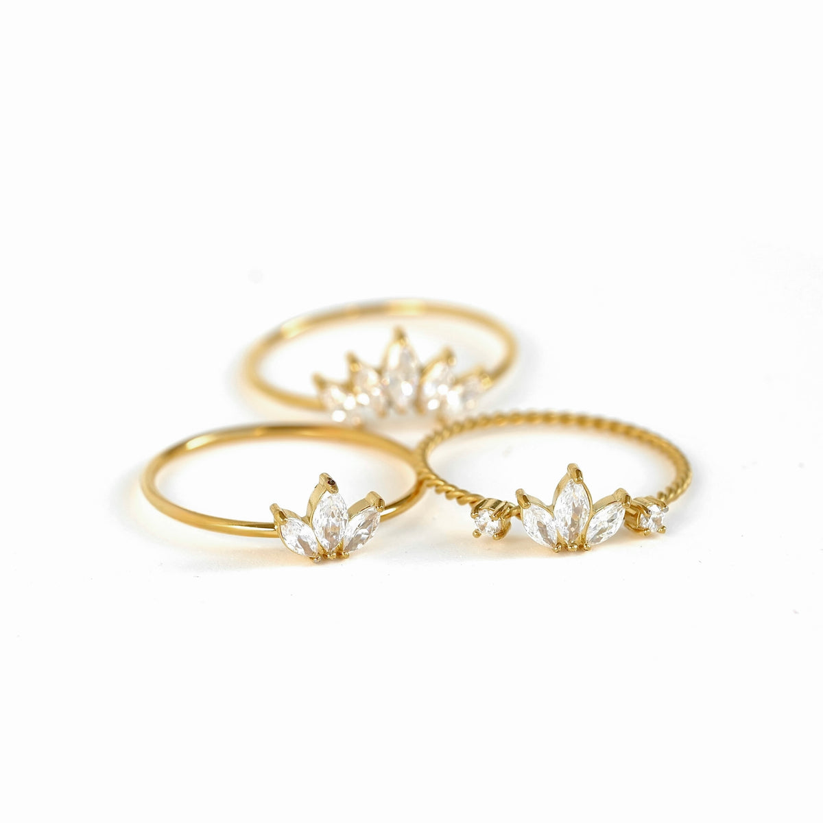 Three gold rings with clear marquise-cut gemstones arranged on a white background.