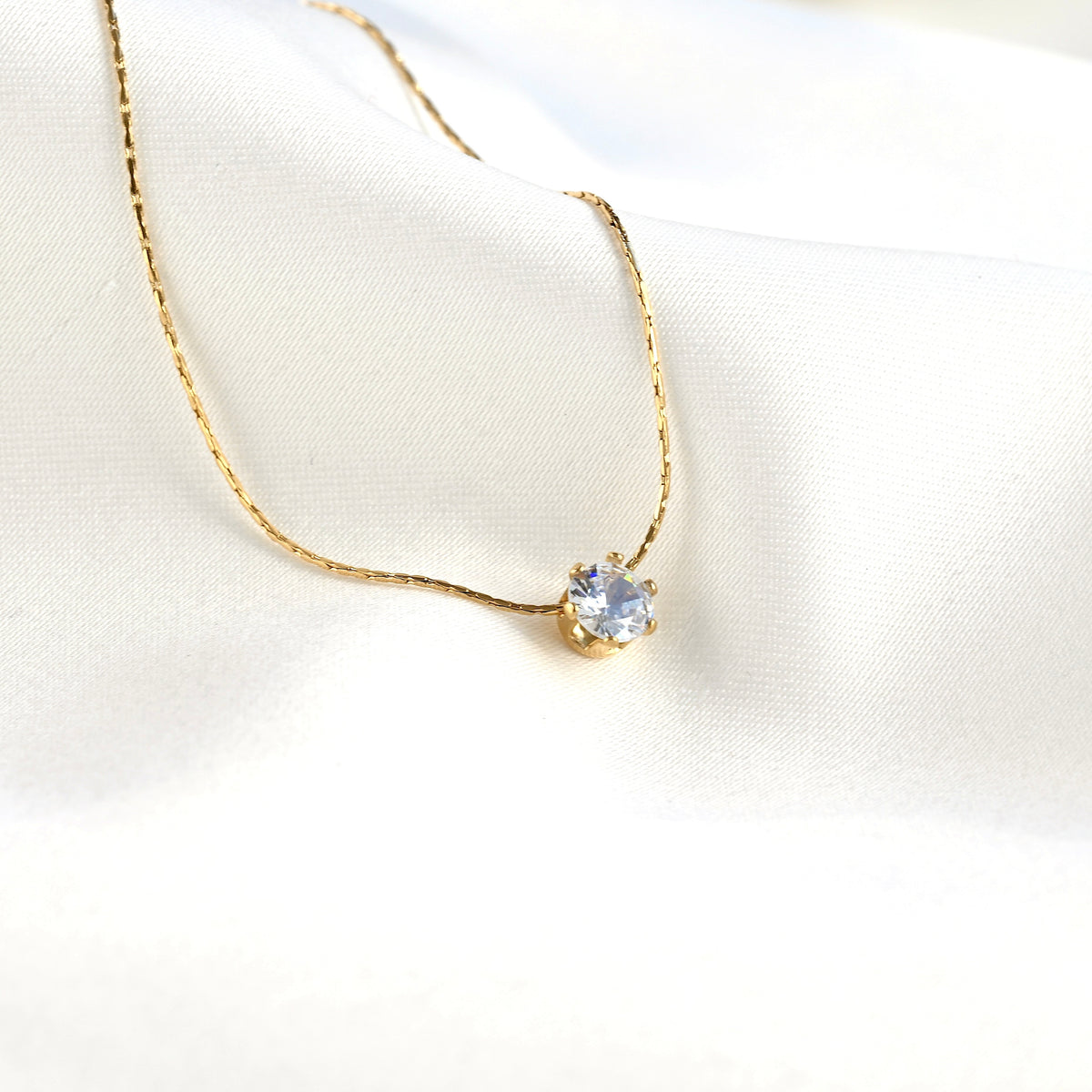 Wide angled view of gold necklace with a clear stone pendant on a white background