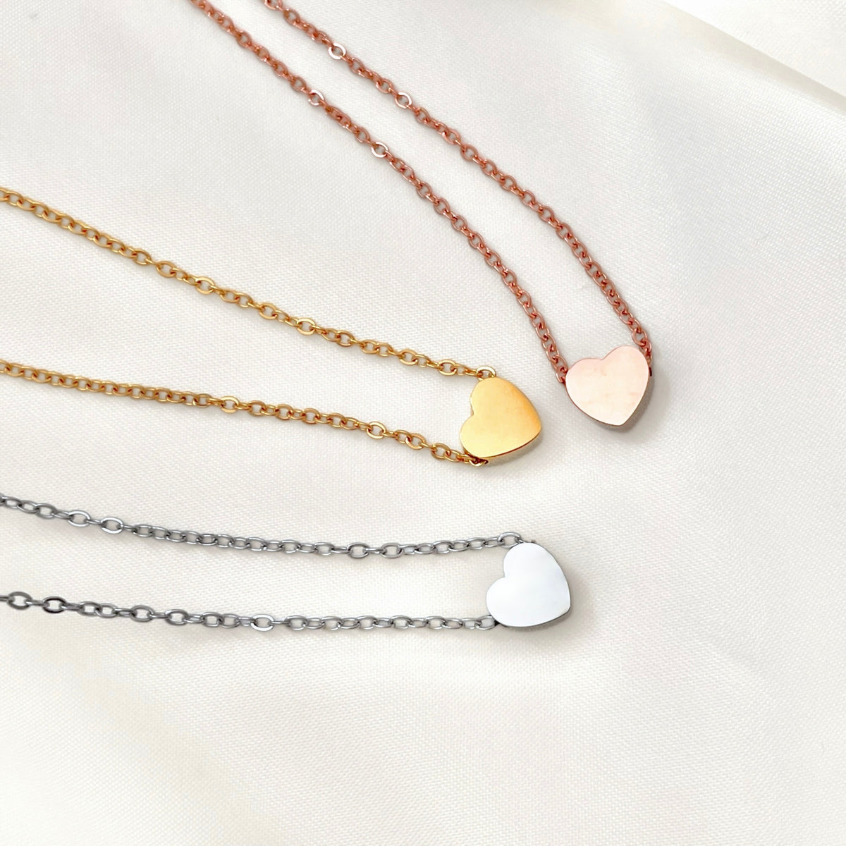 Top view of three mini heart pendants in gold, rose gold, and silver with a finecable chain on a white background