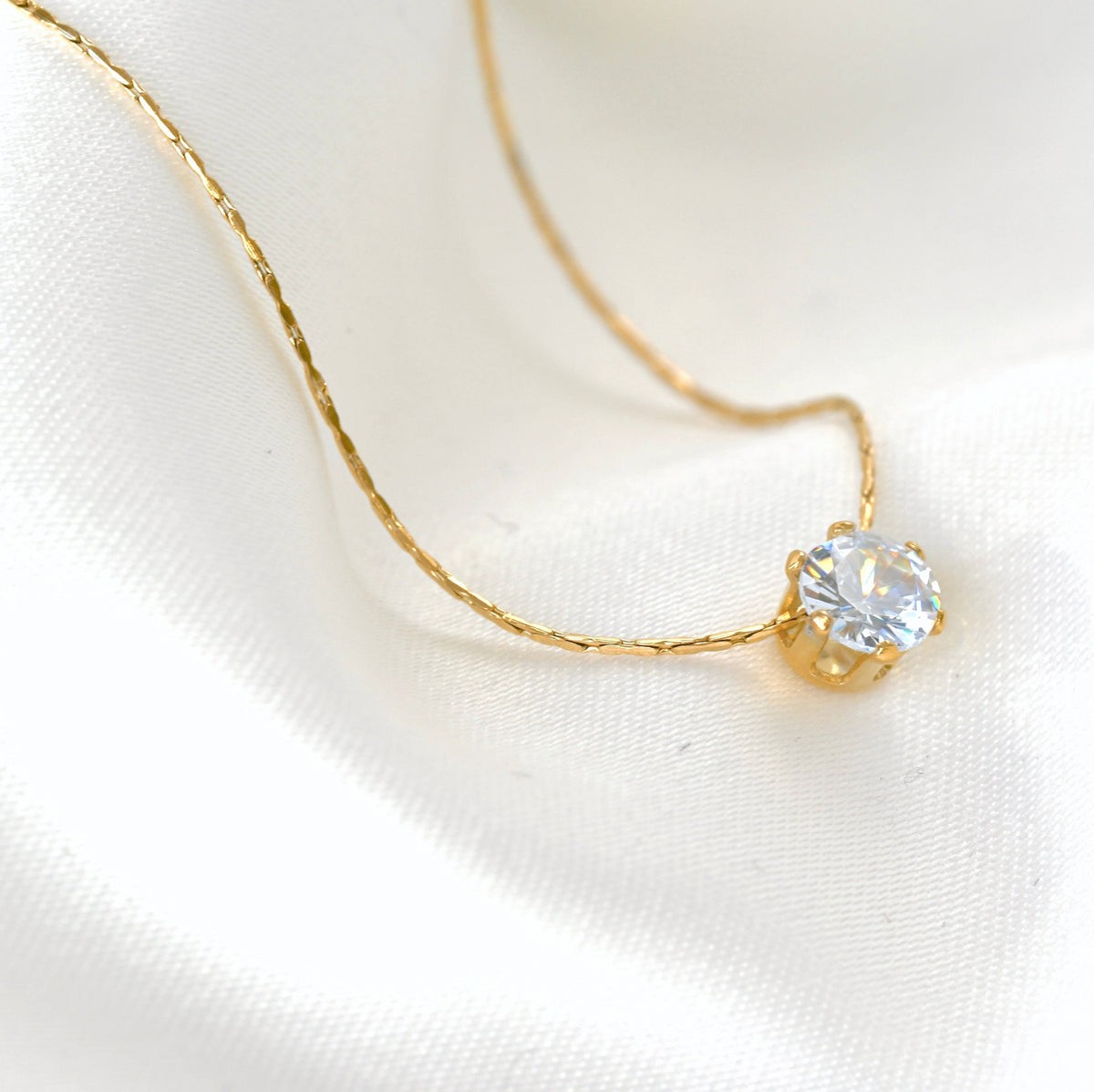 Close-up view of gold necklace with a clear CZ stone showcasing the high clarity of the stone on a white fabric background