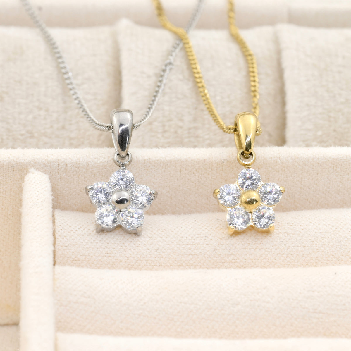 Two flower pendants, one silver and one gold, on a beige fabric background.