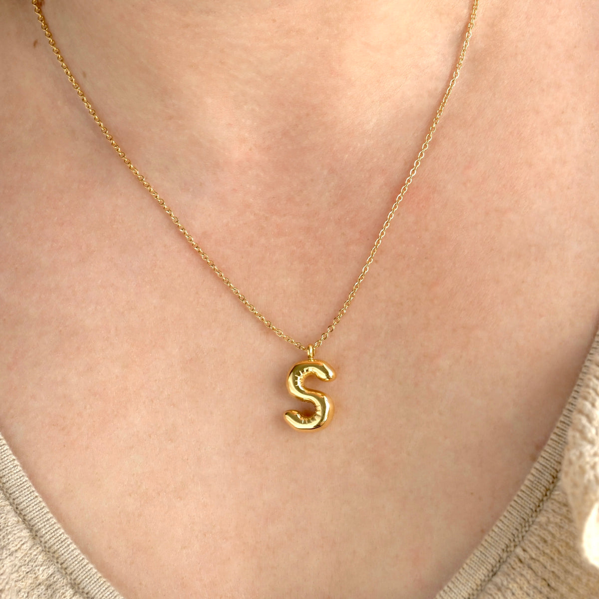 Gold initial necklace with an 'S' pendant on a person's neck