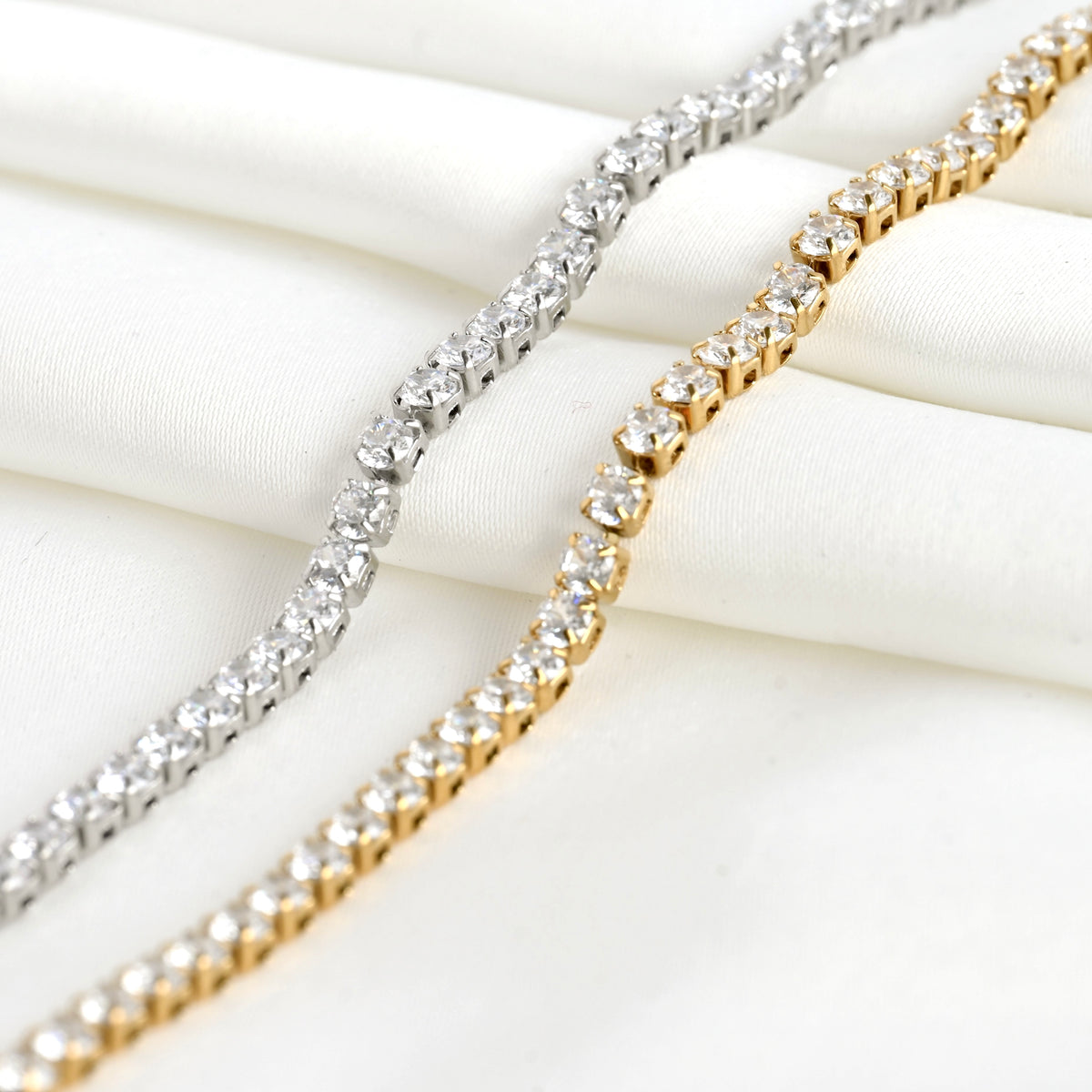 Two diamond bracelets, one silver and one gold, on a white fabric background.