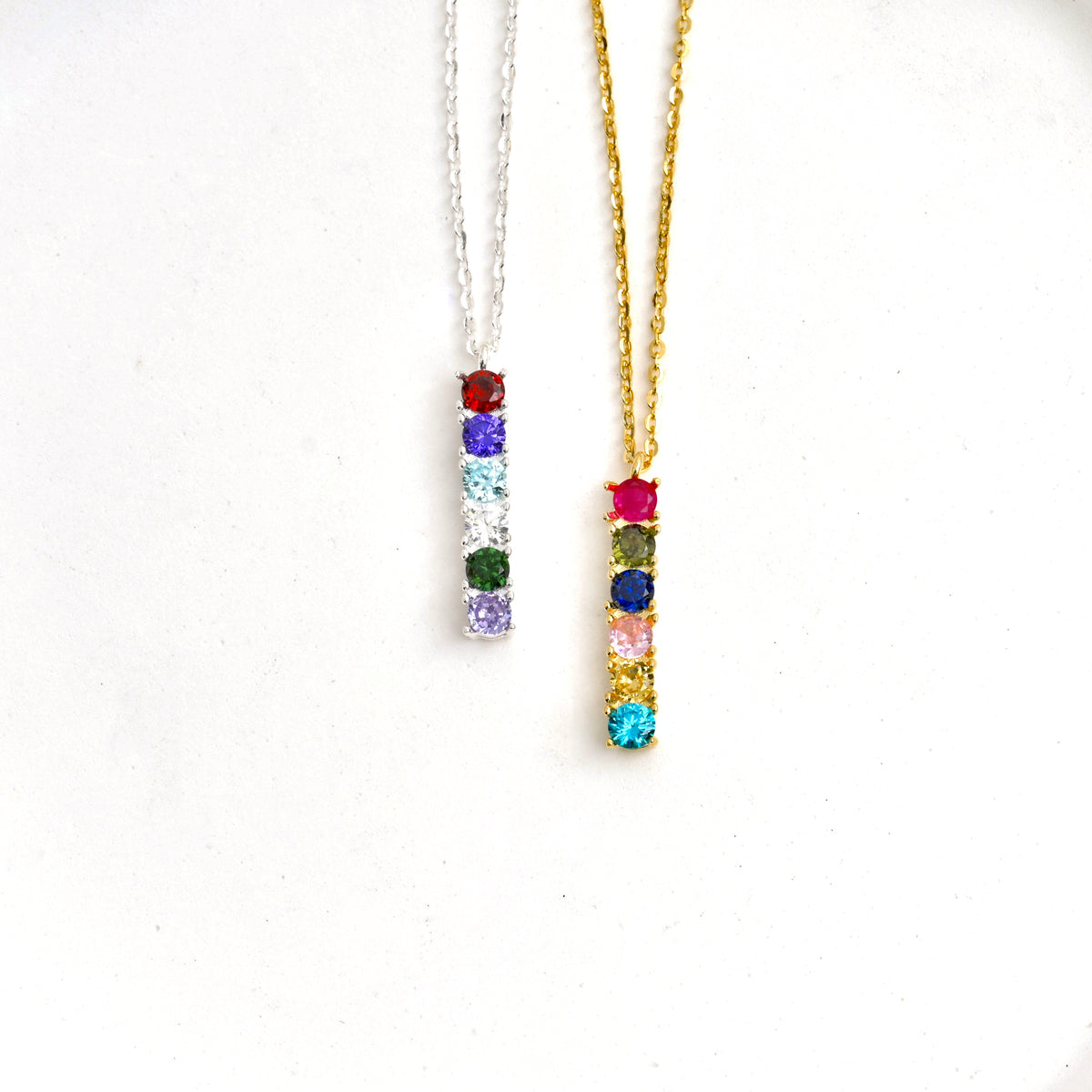 Two personalized birthstone bar necklaces, one gold and one silver, with colorful CZ stones on a white background