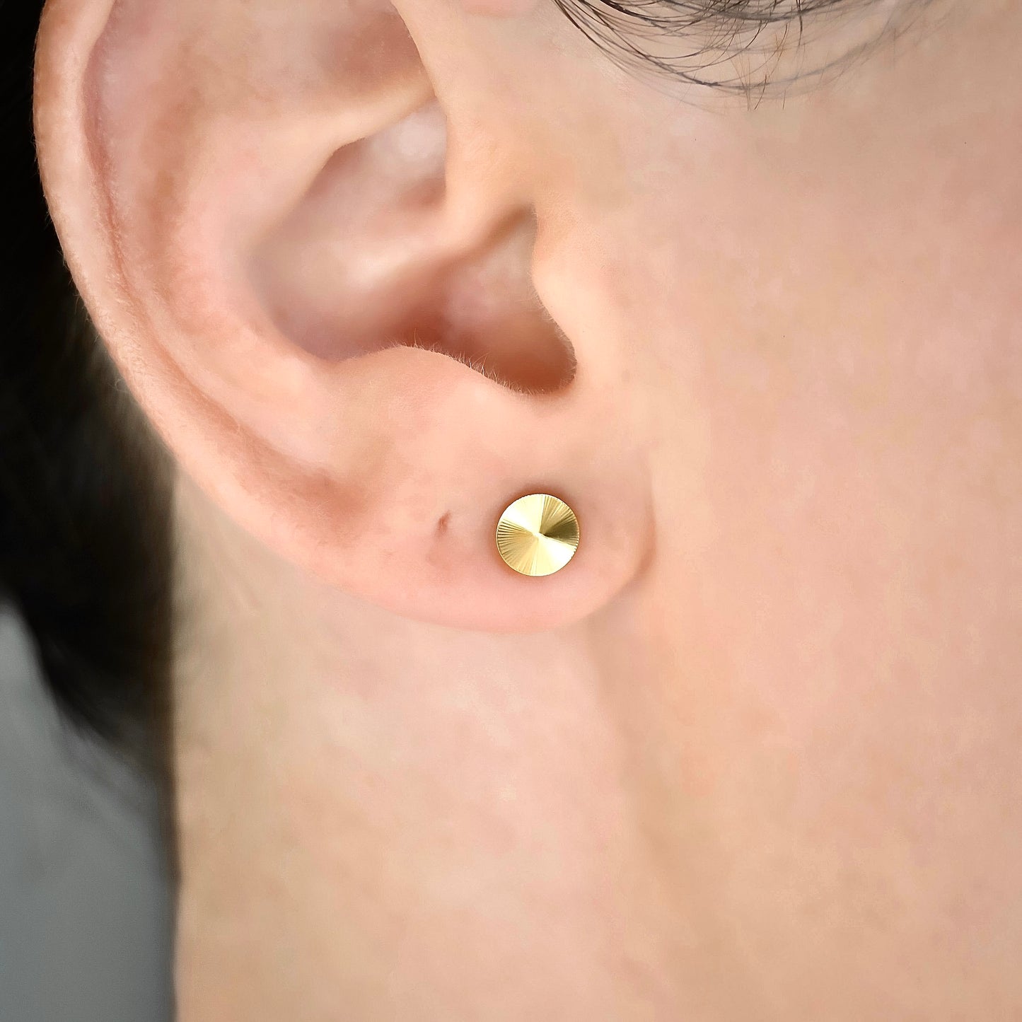 Close up view of gold stud worn on a person's ear with a blurred background