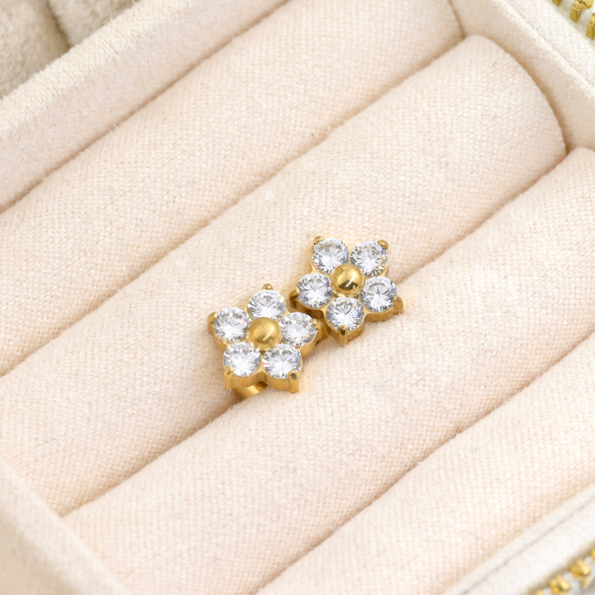 Small gold flower earrings with diamonds in a beige jewelry display tray