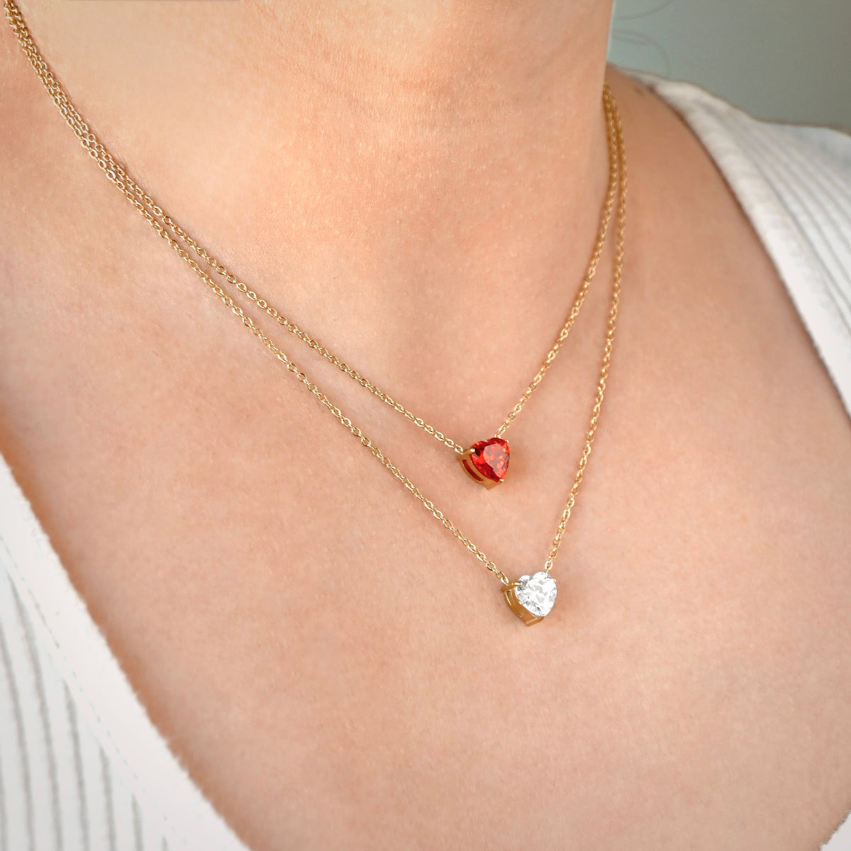 Two gold necklaces with garnet and diamond heart solitaires on a person's neck.
