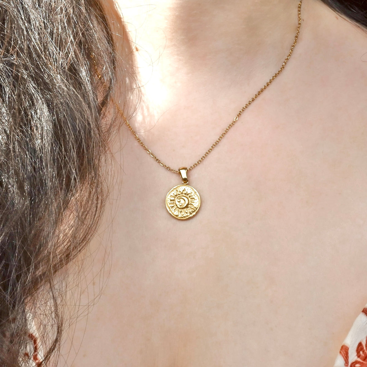 Gold necklace with a circular pendant with an embossed sun and moon worn by a person