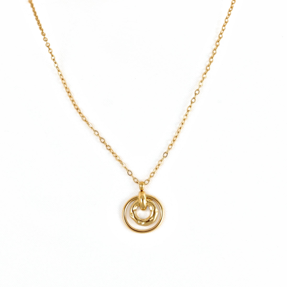 A delicate gold chain necklace featuring a pendant with two interlocking circular rings, one of which has a small heart-shaped cutout, shown against a plain white background.