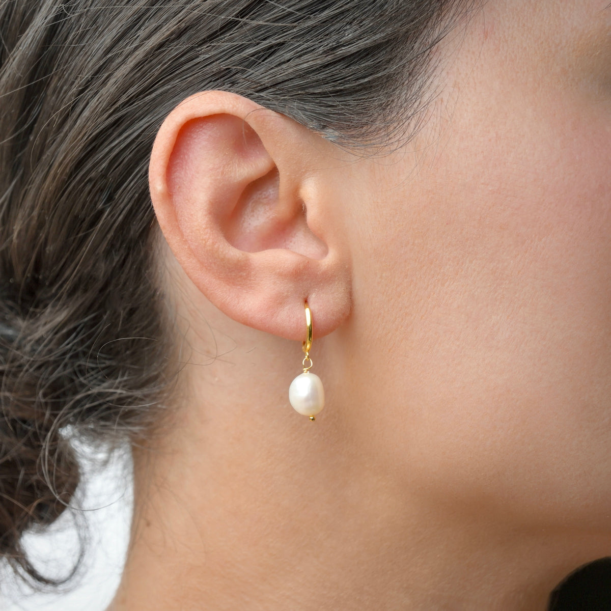 Gold Pearl earring worn by a person with a neutral background