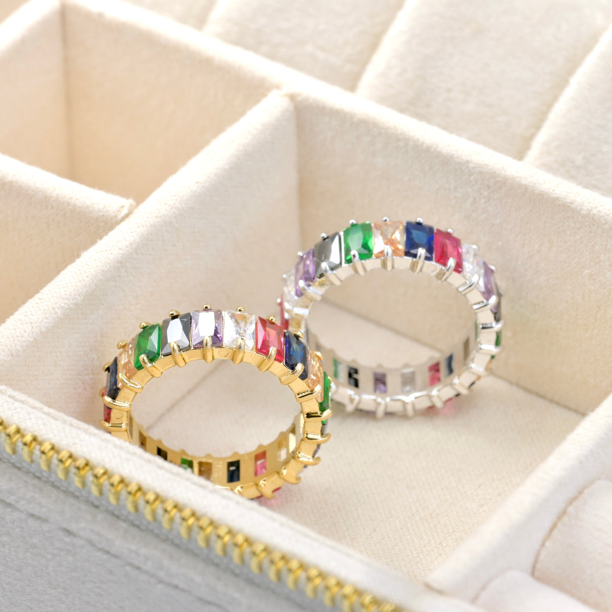 One gold and one silver ring with rainbow colored gemstones in a jewelry box.
