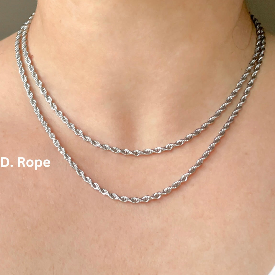 Silver rope chain necklace on a person's neck with a neutral background