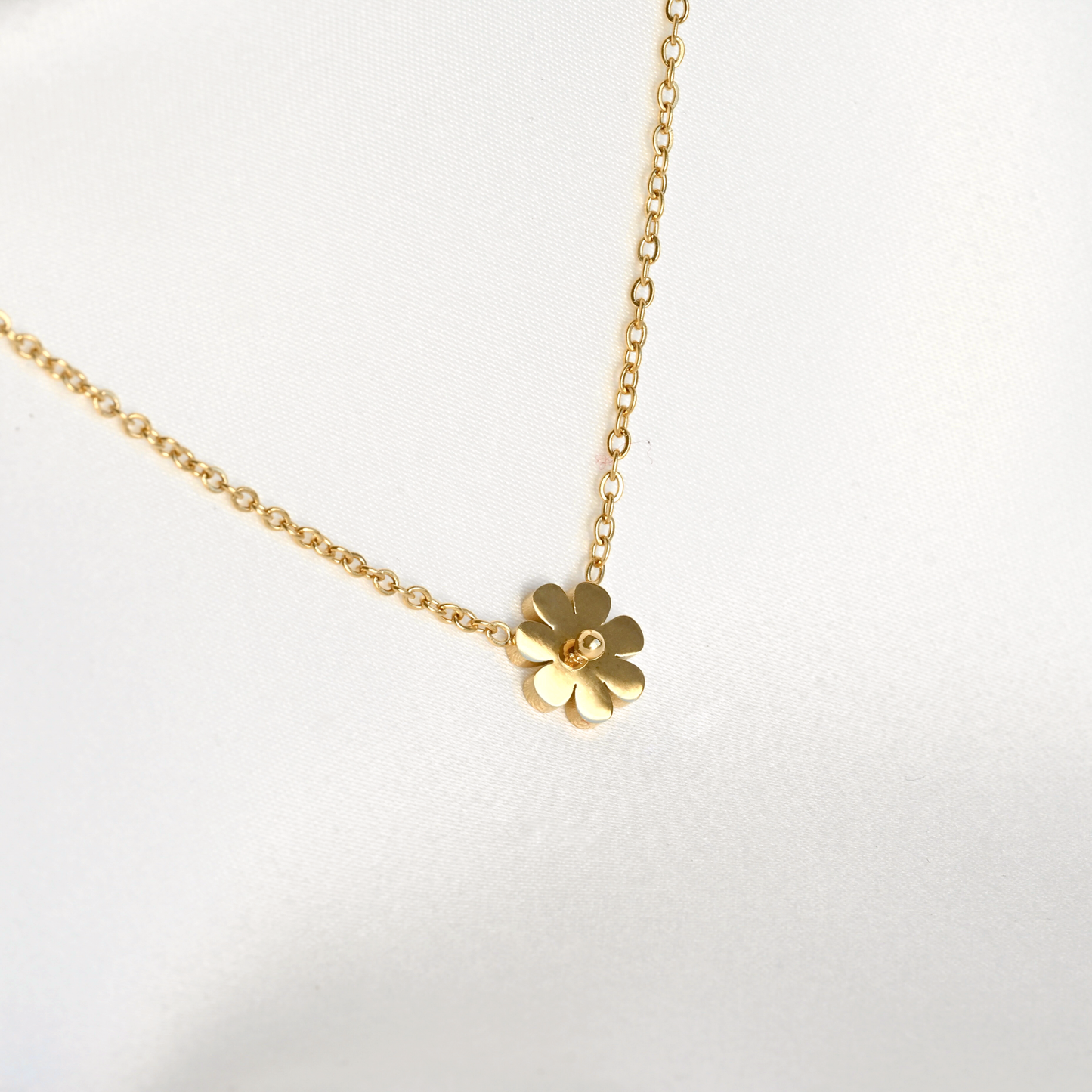 Gold necklace with a flower pendant partially reflecting light on a white background