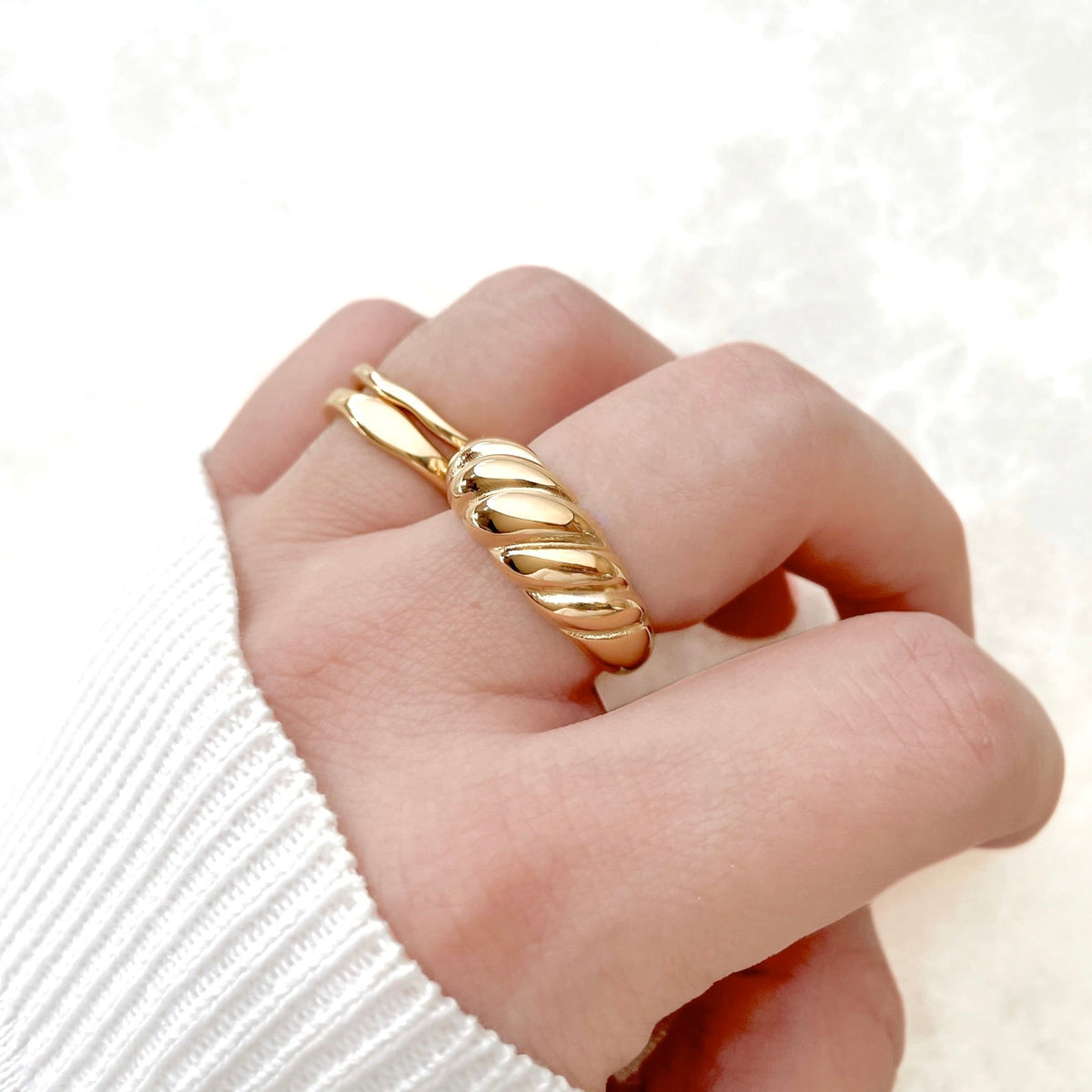 Twisted Gold dome ring on a finger against a white background