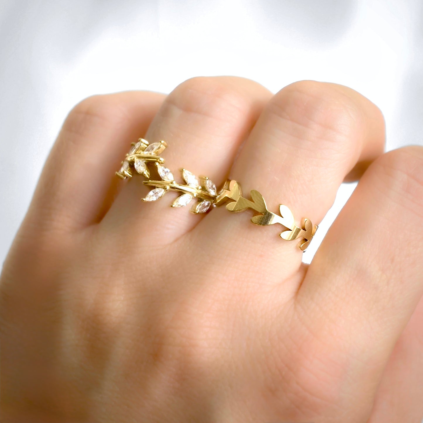 A gold leaf wreath ring worn on a finger, featuring small clear marquise-cut stones set along parts of the wreath, shown on a hand against a bright white background.