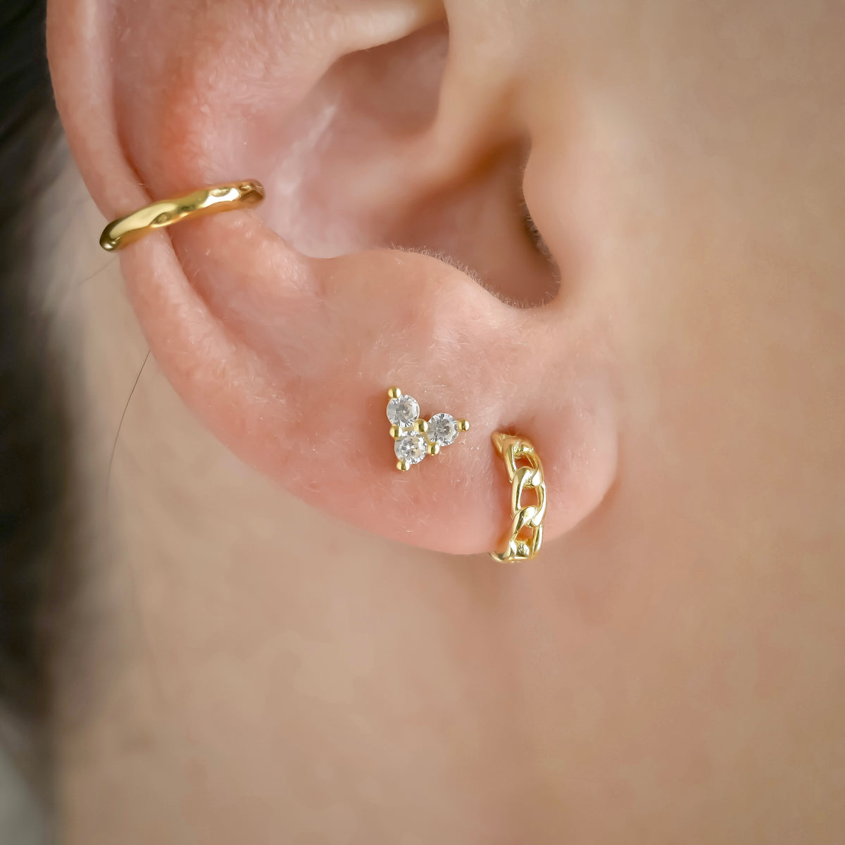 Close-up of an ear wearing gold earring stack with hoops, studs and ear cuffs