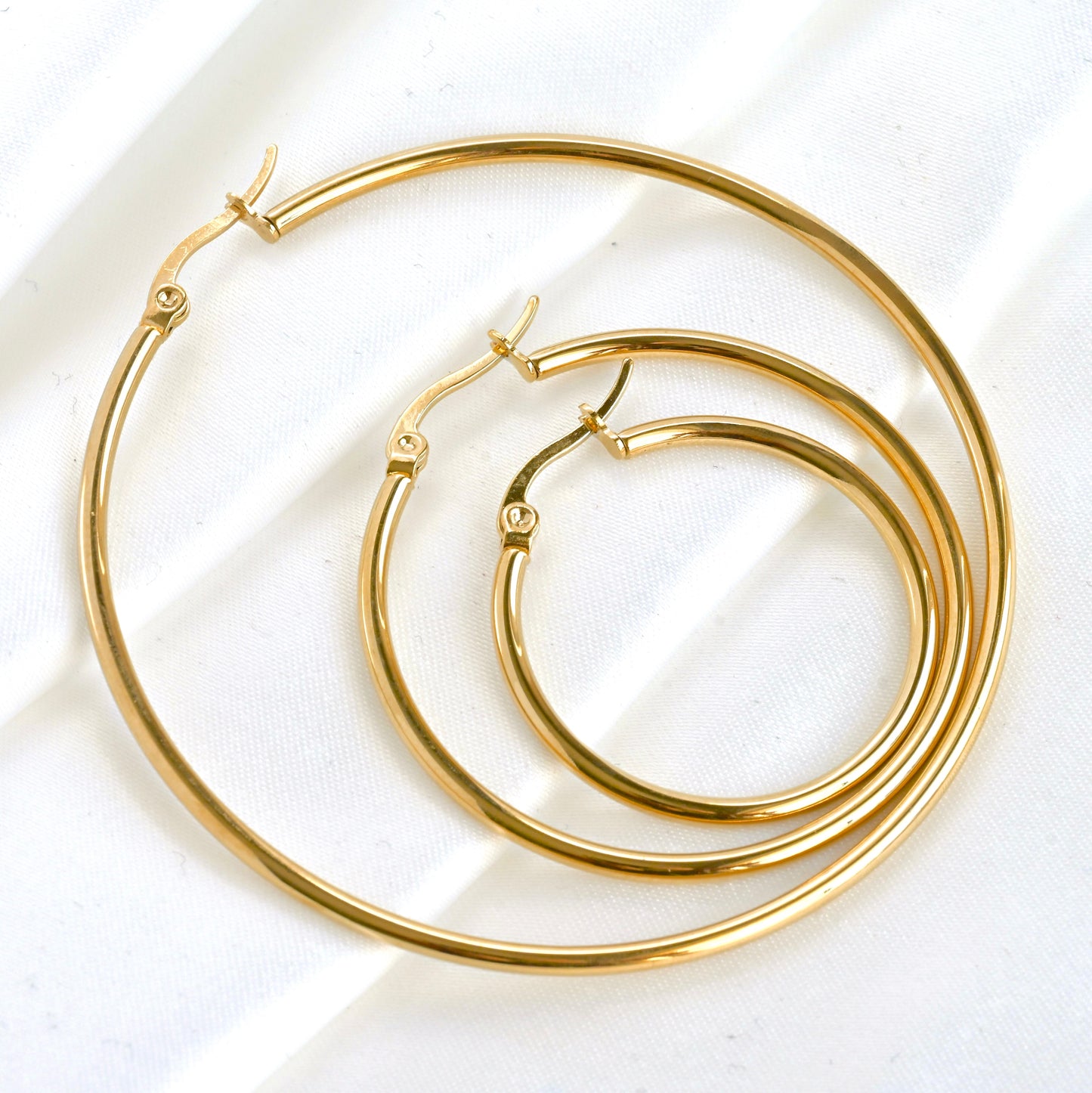 Close-up view of gold hoop earrings in 3 different sizes nested on a white background