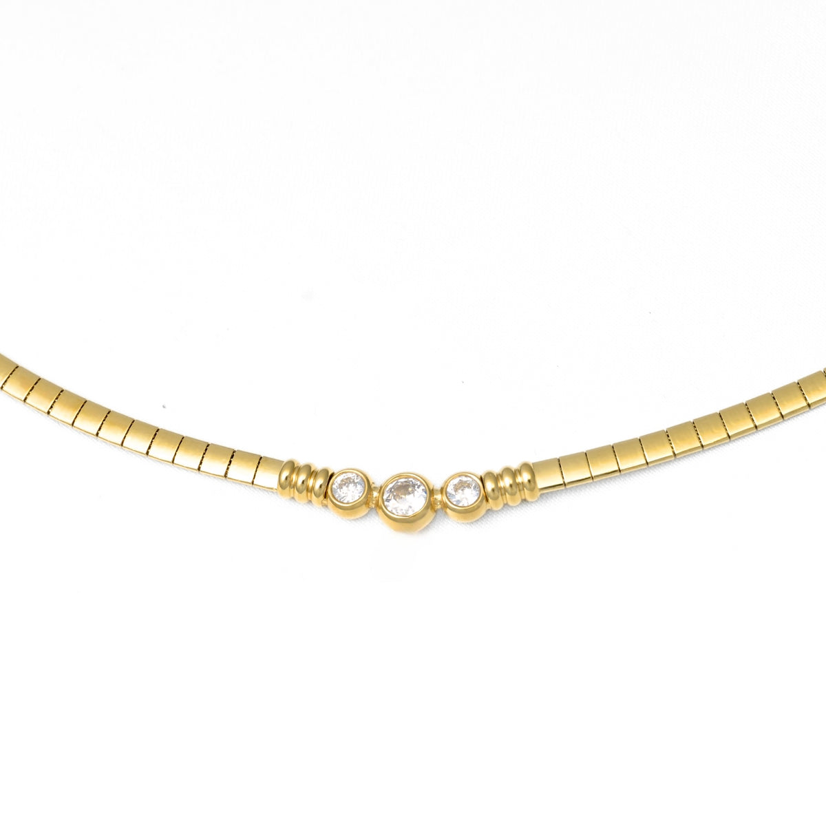 A gold omega chain necklace featuring three small clear round-cut gemstones set in a central cluster, photographed against a plain white background.
