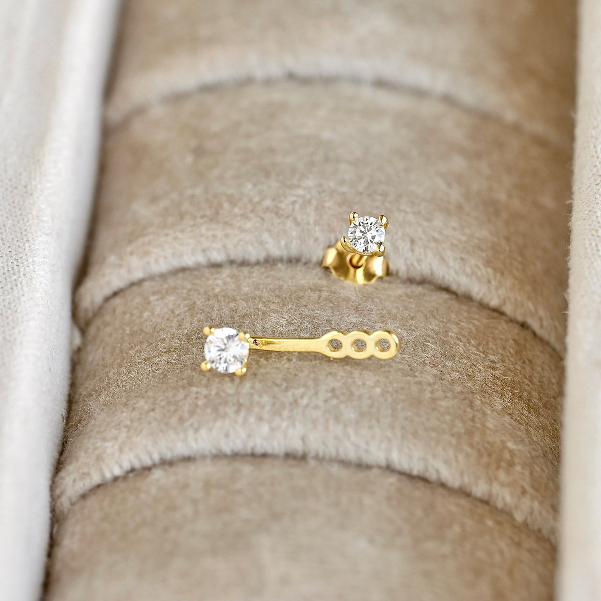 Gold ear jacket with clear CZ stones, one stud with butterfly backing and one jacket style with three slots displayed in a beige jewelry box.