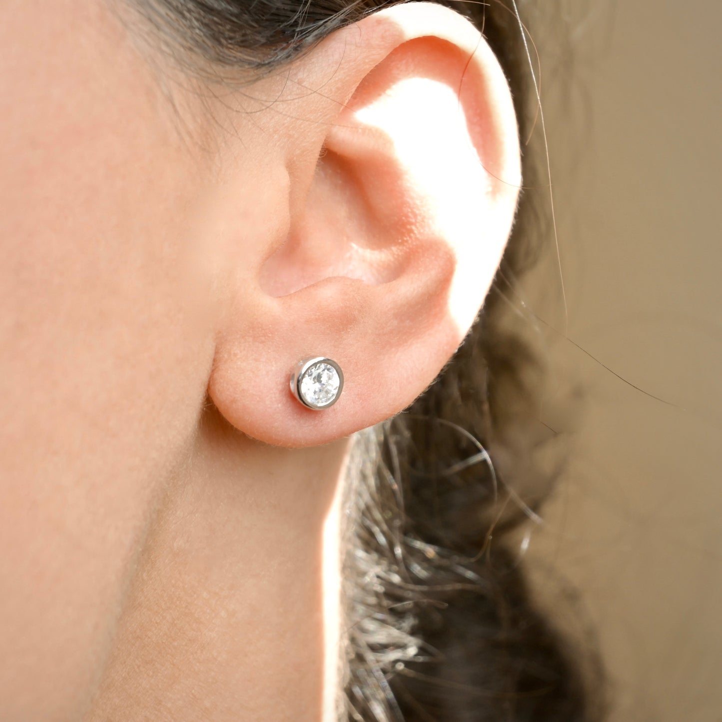 Close-up of an ear wearing a silver diamond earring with a white stone.