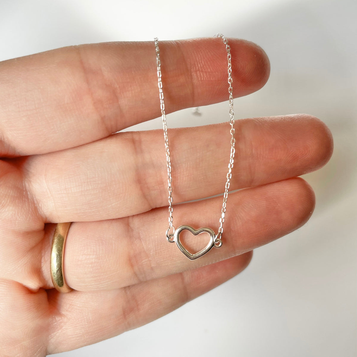 Silver heart bracelet with a delicate chain held in a hand against a white background