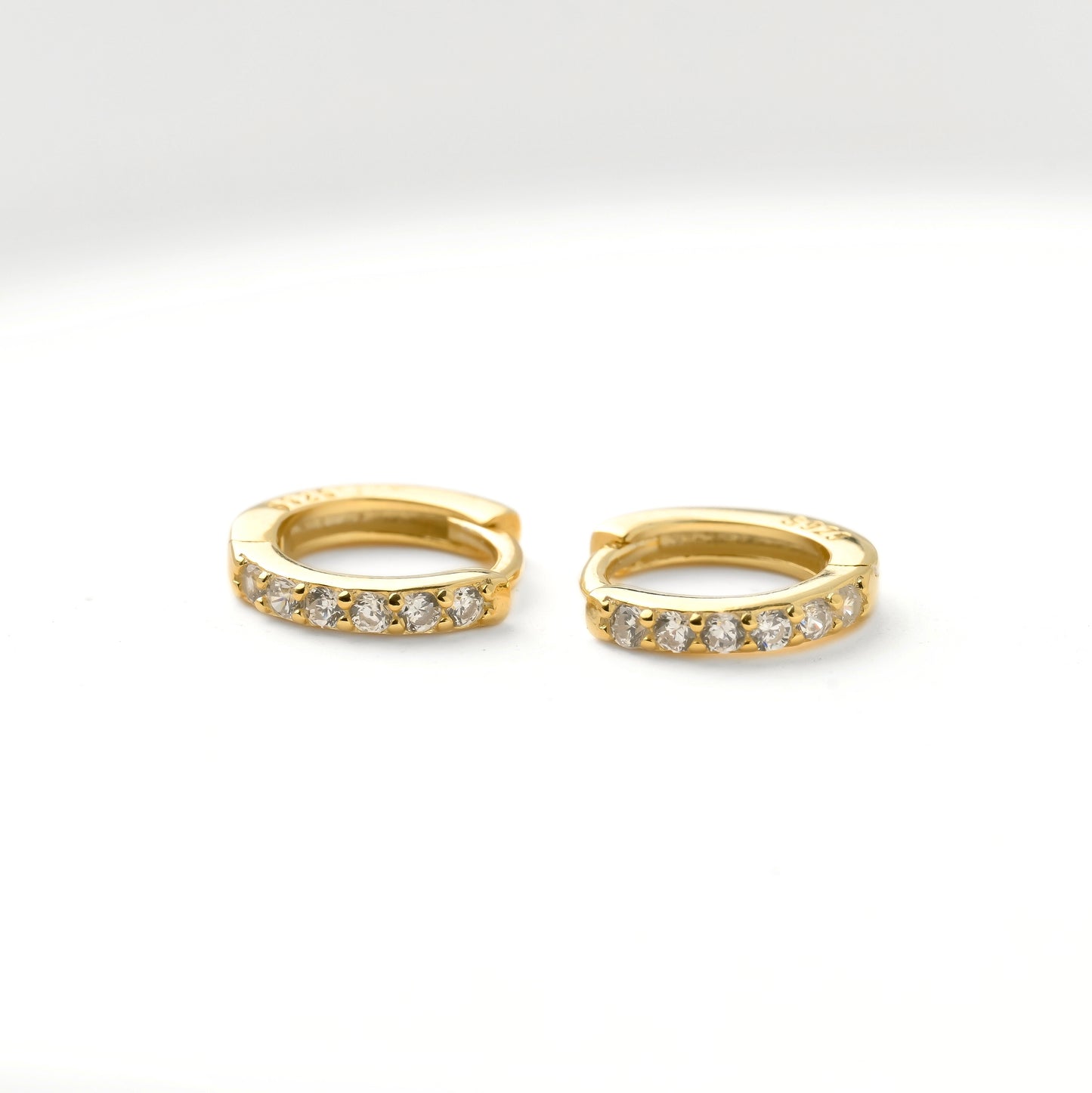Gold huggie hoop earrings with embedded diamonds and S925 hallmark stamp on a white background