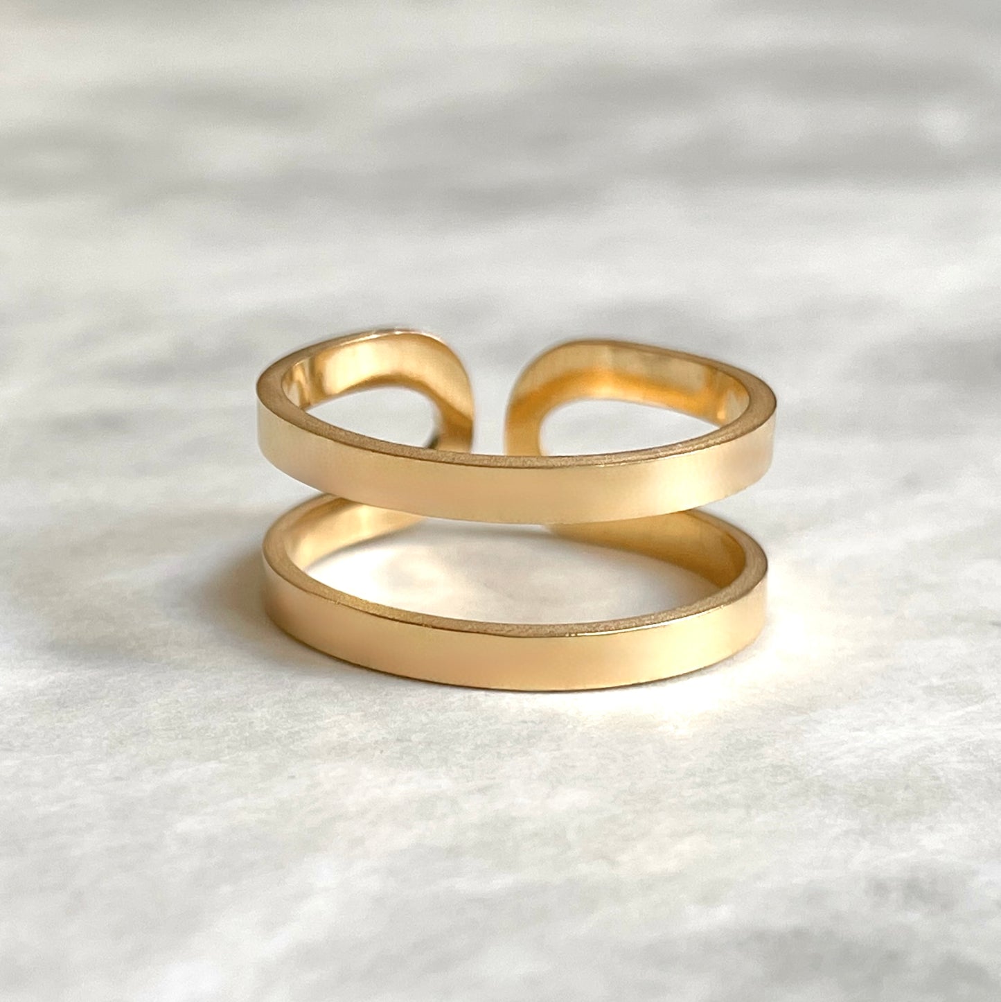 Front view of bold adjustable ring in gold on a textured white surface