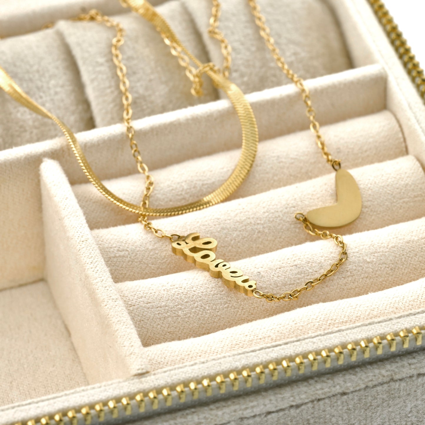 Gold herringbone and cable necklaces with heart and love pendants on a beige jewelry display box.