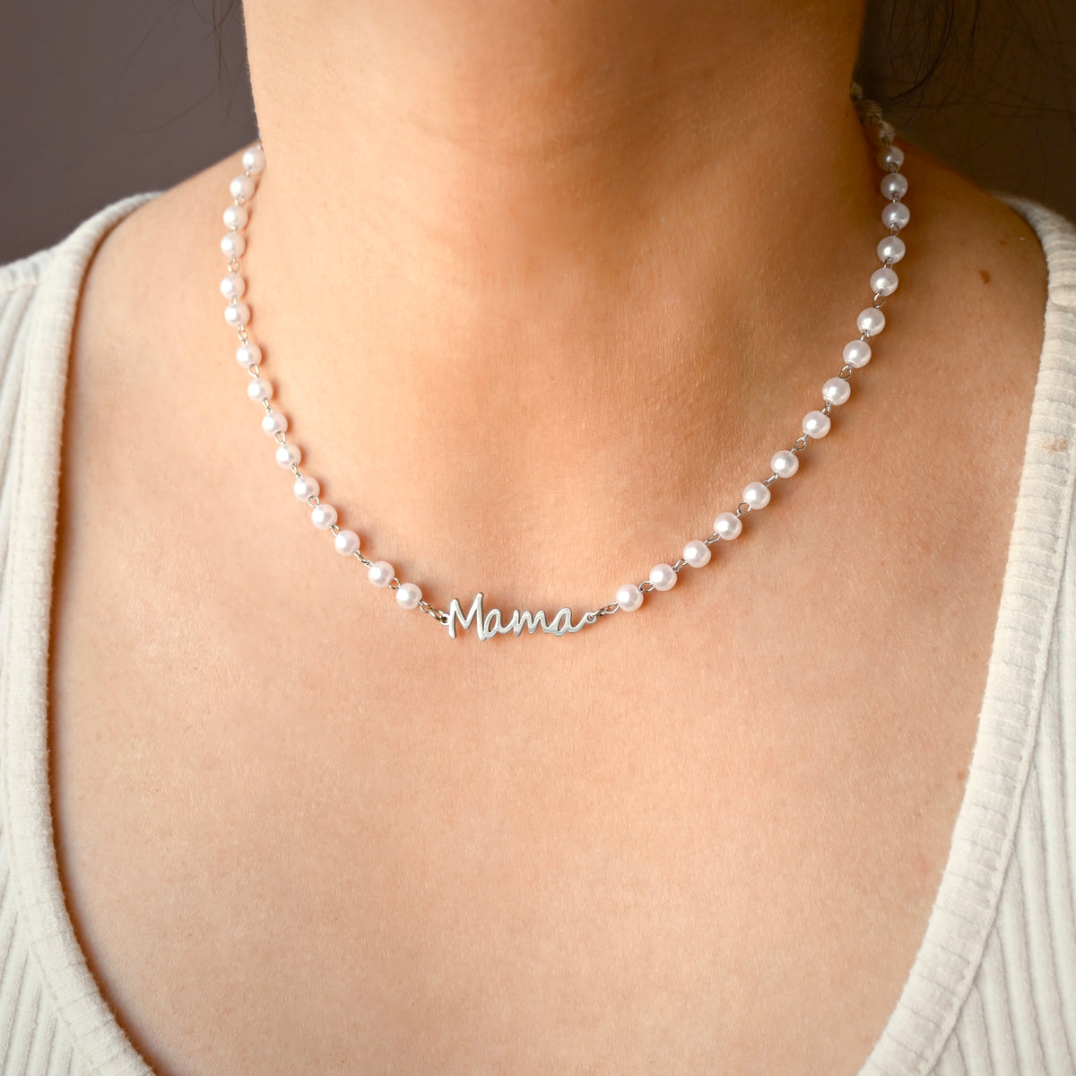 A close-up of a person wearing a pearl necklace with a silver script nameplate that reads 'Mama'.