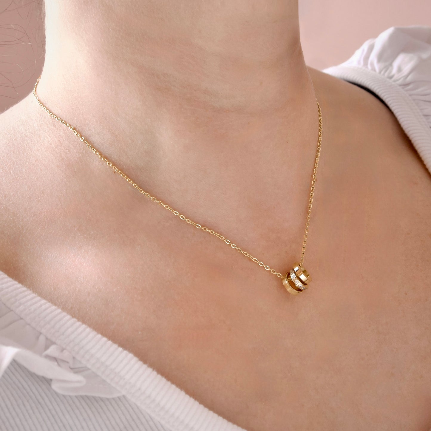 A delicate gold chain necklace with a small gold ring trio pendant, worn on a model's neck over a white top.