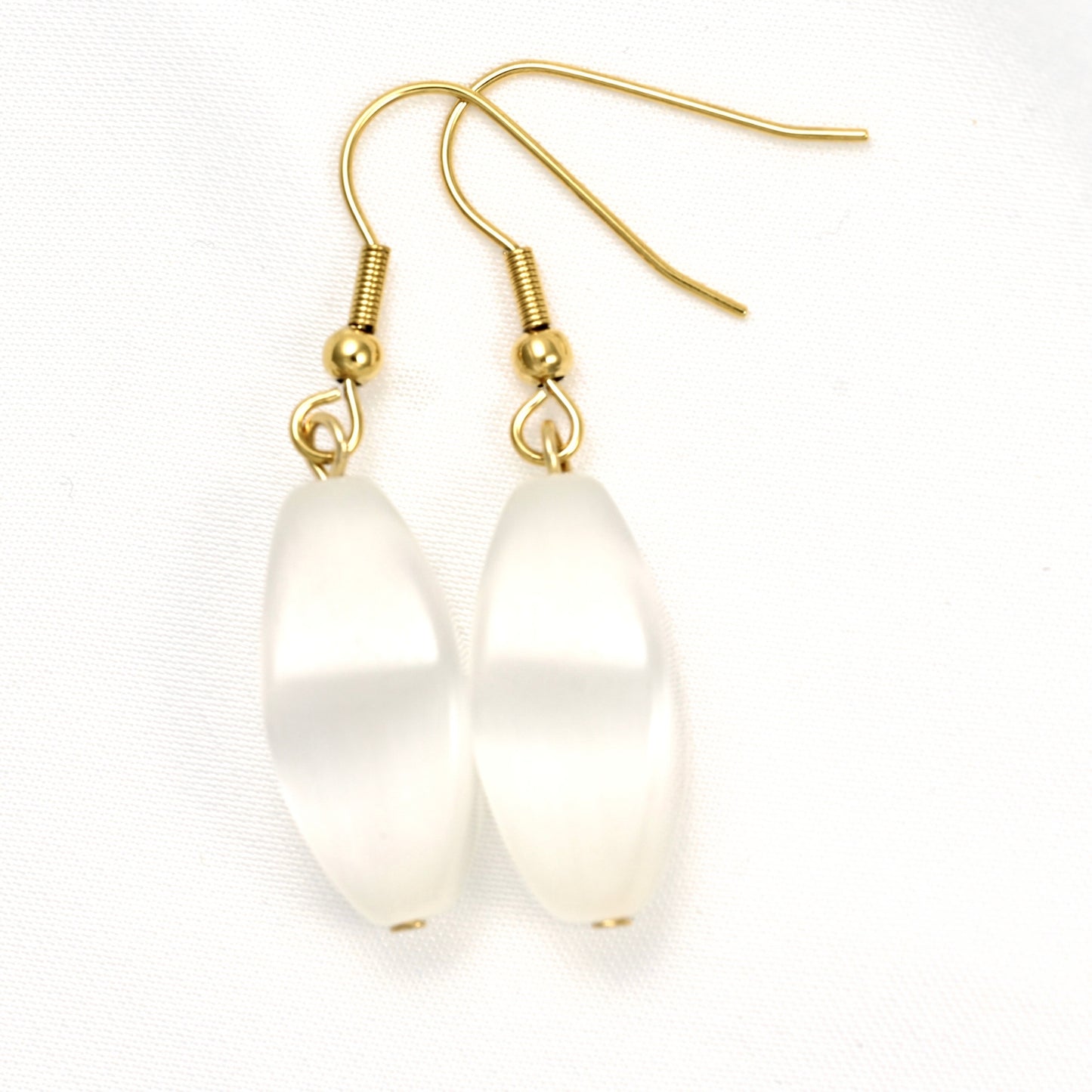 A pair of dangle earrings with smooth, teardrop-shaped milky white crystals and gold-tone fishhook wires, shown on a textured white background.