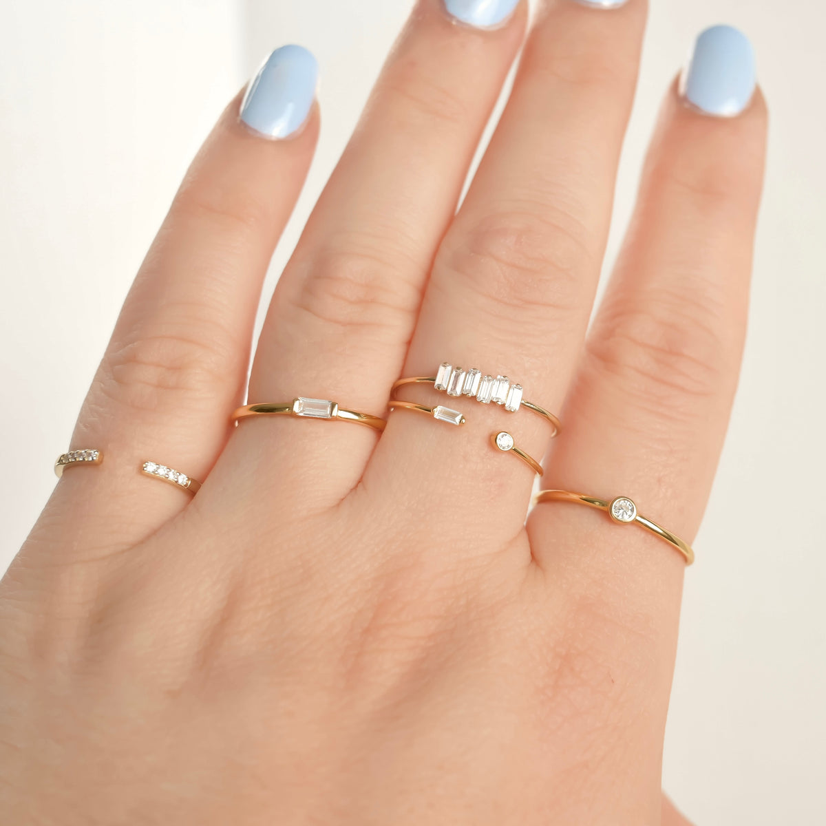 Hand wearing multiple gold rings with small gemstones on a light background