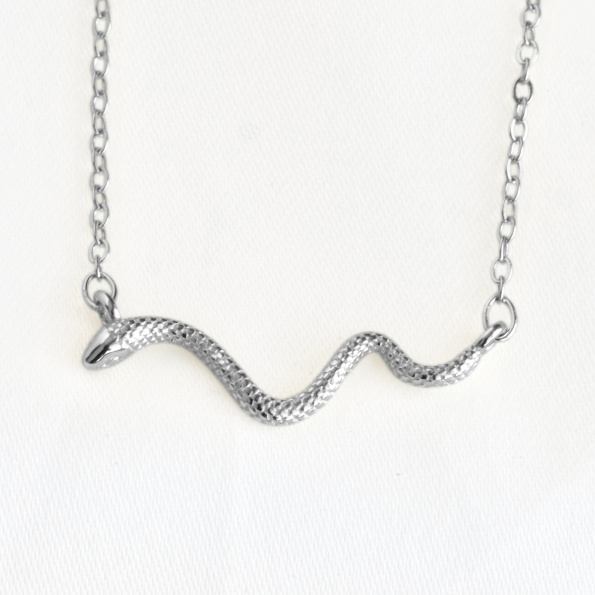 A silver snake pendant necklace with a textured scale finish, suspended from a delicate silver link chain against a plain white background.