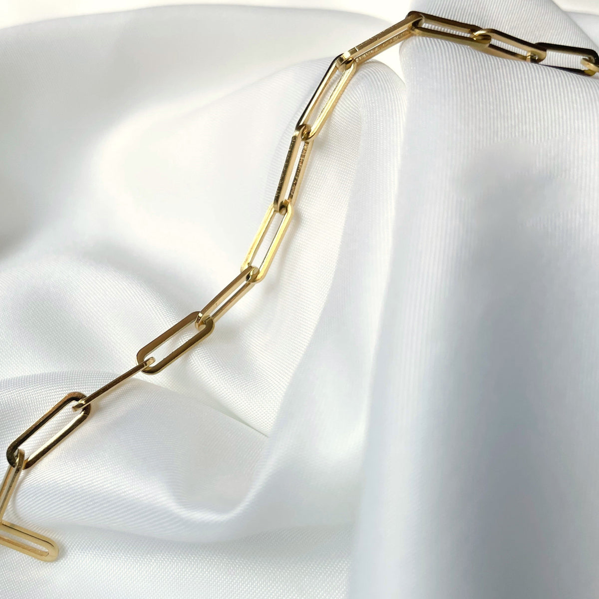 Gold paperclip chain necklace on a white fabric background